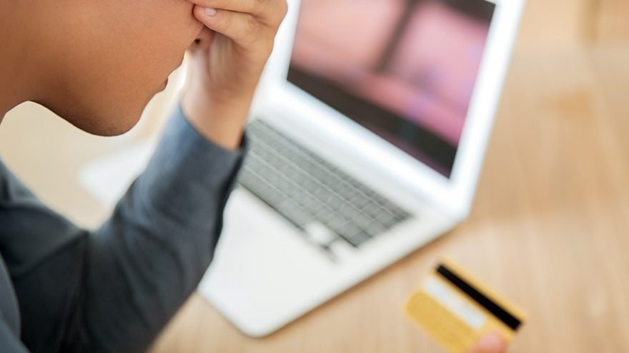 Pessoa preocupada diante de um notebook segurando um cartão bancário